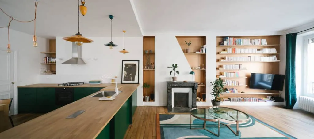 Vue panoramique d’un séjour ouvert avec cuisine à îlot vert, cheminée en marbre et bibliothèque sur mesure