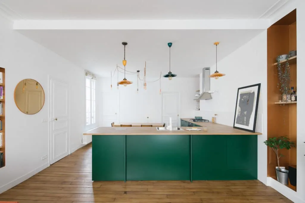 Cuisine ouverte sur mesure avec îlot vert et plan de travail en bois dans un appartement rénové à Paris.