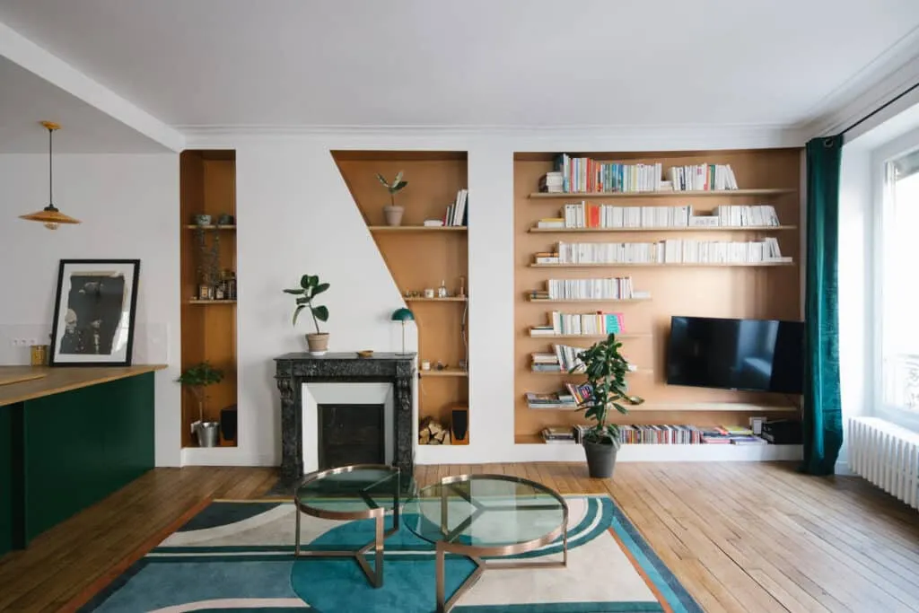 Salon lumineux avec bibliothèque encastrée sur mesure en bois clair, cheminée en marbre noir et parquet ancien