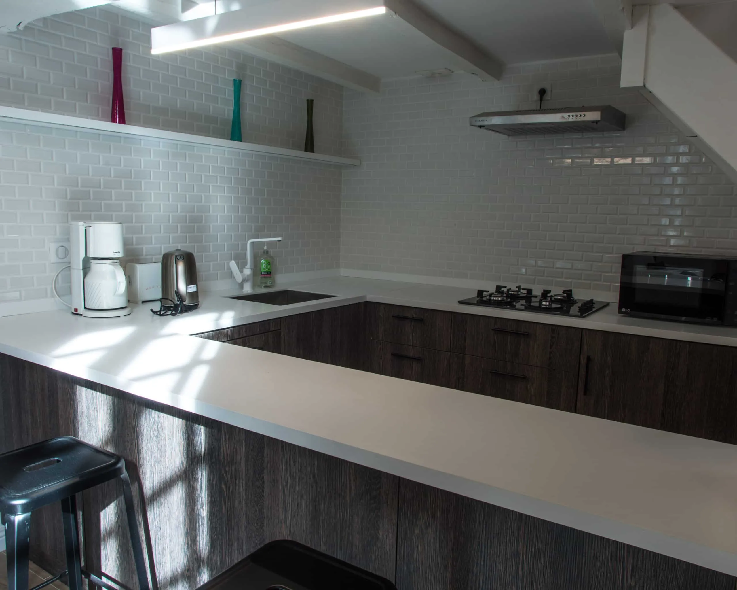 Cuisine en U aux façades de bois foncé et plan de travail blanc avec bar, crédence en carrelage métro blanc et tabourets noirs
