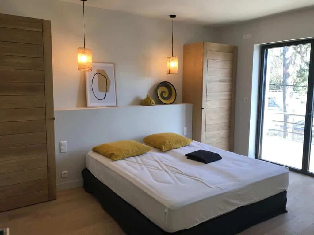 Chambre avec lit double aux coussins jaunes, placards en chêne et suspensions en rotin