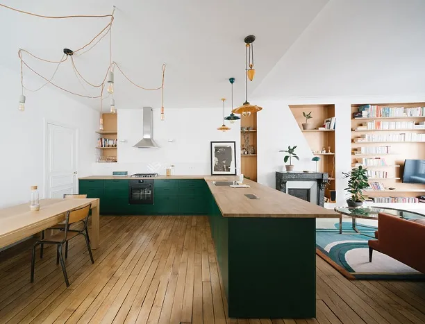Grand séjour lumineux avec cuisine ouverte aux façades vertes et plan de travail en bois, parquet ancien et bibliothèques sur mesure