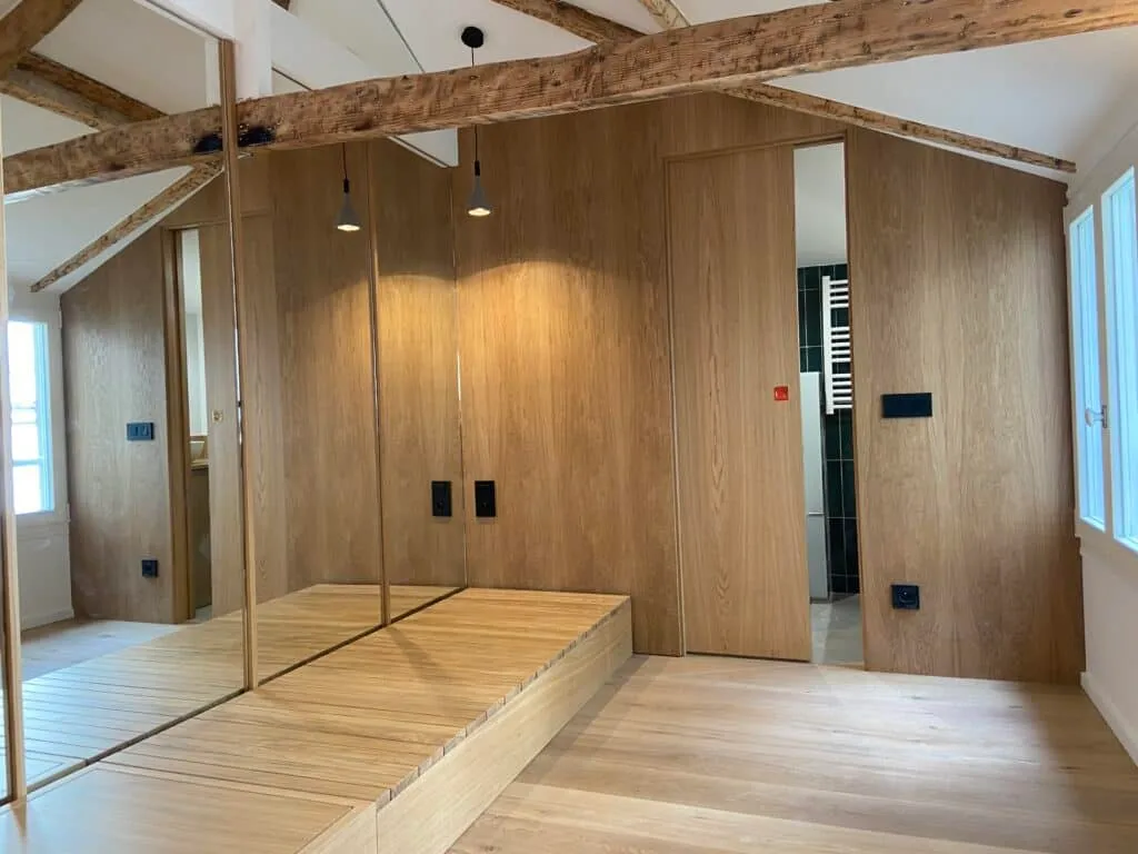 Pièce sous combles rénovée avec poutres apparentes, panneaux en chêne sur mesure et estrade en bois